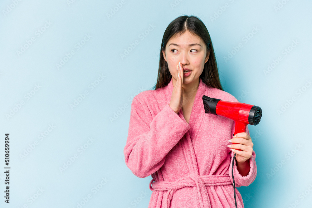 Young asian woman wearing a bathrobe and holding hairdryer isolated on pink background is saying a secret hot braking news and looking aside Young asian woman wearing a bathrobe and holding hairdryer isolated on pink background is saying a secret hot braking news and looking aside
