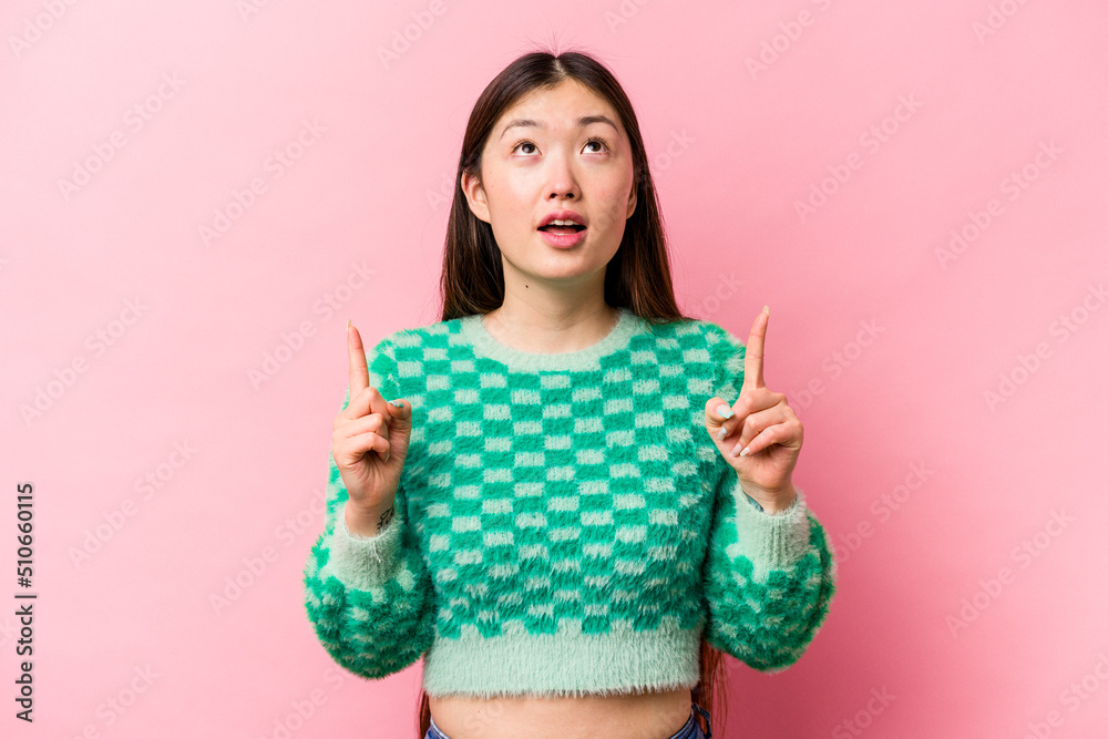 Young Chinese woman isolated on pink background pointing upside with opened mouth. Young Chinese woman isolated on pink background pointing upside with opened mouth.