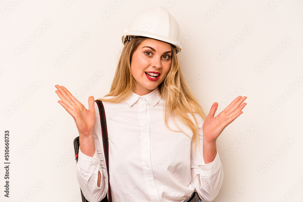 Young architect woman with helmet and holding blueprints isolated on white background surprised and shocked.