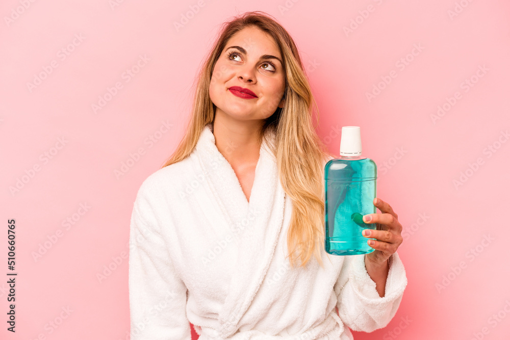 Young caucasian woman holding mouthwash wearing bathrobe isolated on pink background dreaming of achieving goals and purposes Young caucasian woman holding mouthwash wearing bathrobe isolated on pink background dreaming of achieving goals and purposes