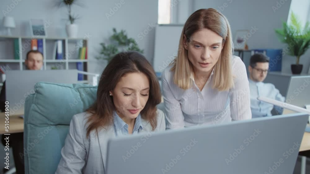 Two young businesswomen working discussing use laptop computer In modern office . On background people working. Portrait. Close up Two young businesswomen working discussing use laptop computer In modern office . On background people working. Portrait. Close up