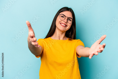 Young caucasian woman isolated on blue background feels confident giving a hug to the camera. © Asier