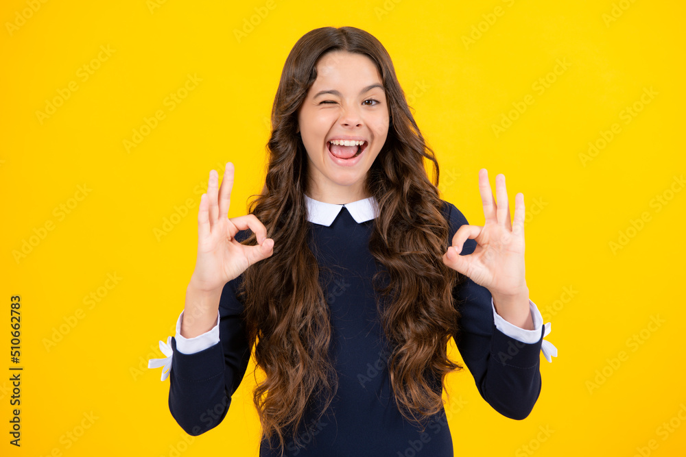 Excited face. Smiling teen girl, young teenager showing ok hand sign and winking looking at camera isolated on yellow studio background. Amazed expression, cheerful and glad. Excited face. Smiling teen girl, young teenager showing ok hand sign and winking looking at camera isolated on yellow studio background. Amazed expression, cheerful and glad.