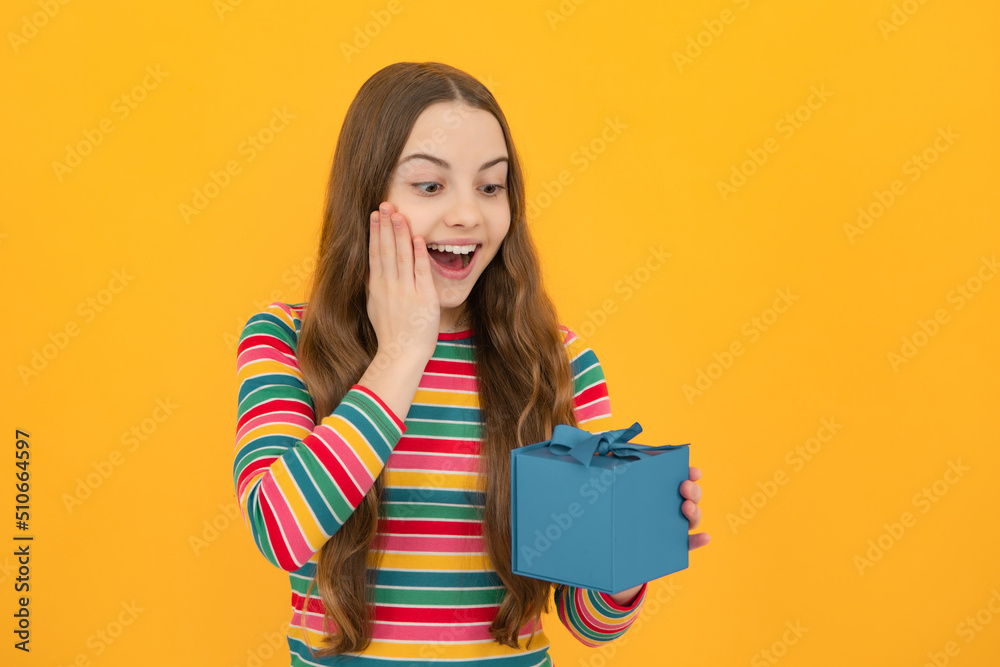 Teenager child holding gift box on yellow isolated background. Gift for kids birthday. Christmas or New Year present box. Excited face, cheerful emotions of teenager girl. Teenager child holding gift box on yellow isolated background. Gift for kids birthday. Christmas or New Year present box. Excited face, cheerful emotions of teenager girl.