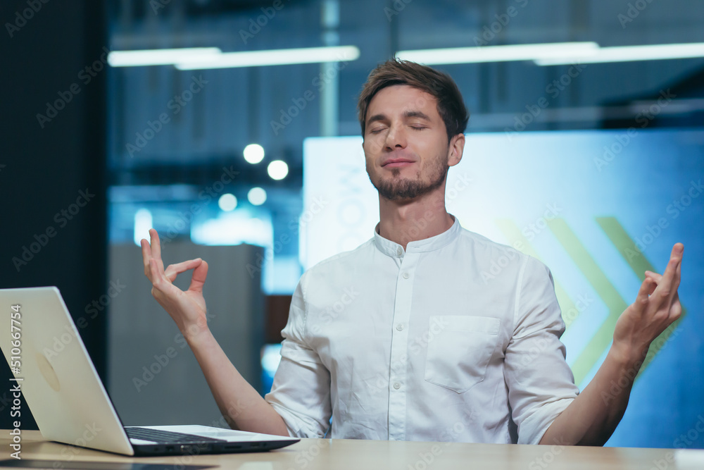 Fototapeta premium Business man working in a modern office, meditating and practicing yoga at the table, relaxing and calming relieves stress