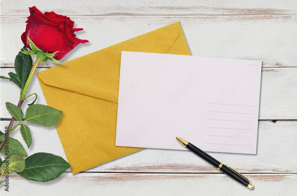 A craft envelope with an empty white postcard and a red rose on a white wooden background. Flat lay. Copy space. Mock up. The concept of Valentine's Day, Birthday and wedding invitation