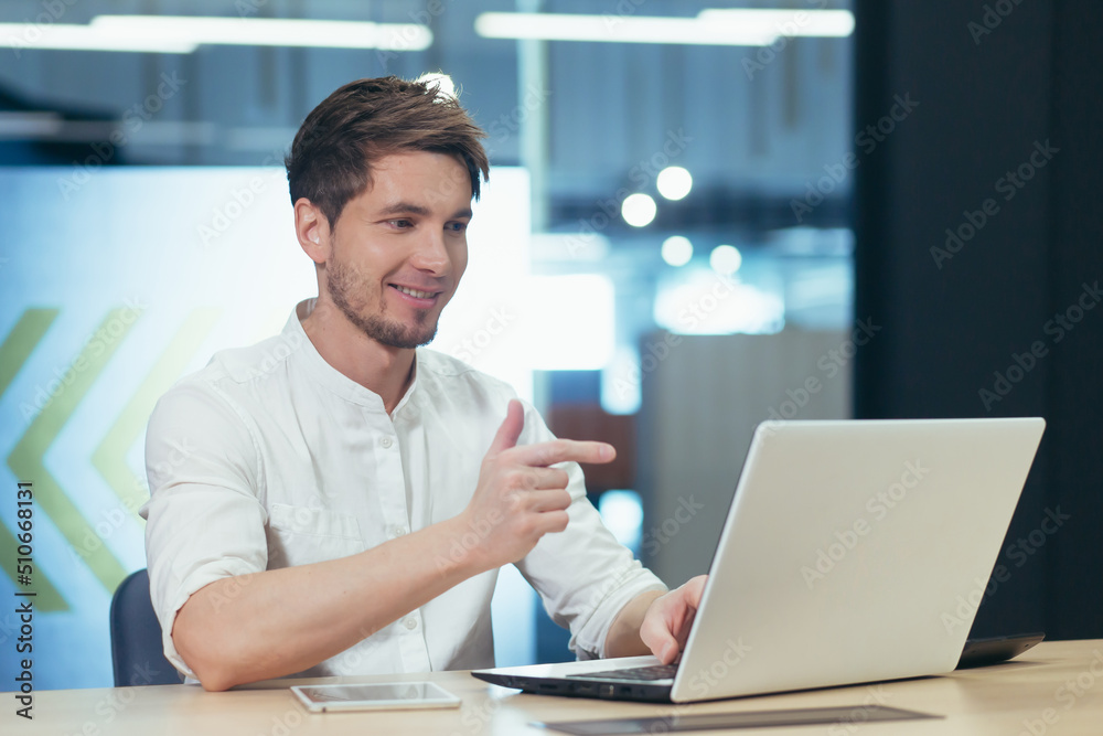 A man in the office works on a laptop, talks on a video call, looks at the screen and smiles at the interlocutor A man in the office works on a laptop, talks on a video call, looks at the screen and smiles at the interlocutor