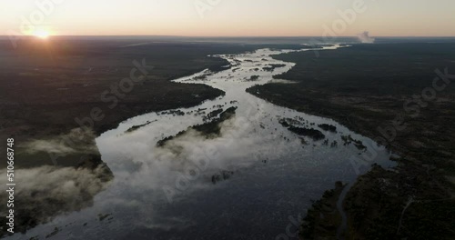 High aerial sunrise fly over view of the mist on the mighty Zambezi River flowing down to the Victoria Falls, Unesco world heritage site