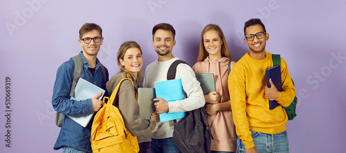 Diverse group of smiling university or college students. Happy multi ethnic young friends in casual wear with backpacks, class textbooks and modern laptop PCs standing together and looking at camera photo