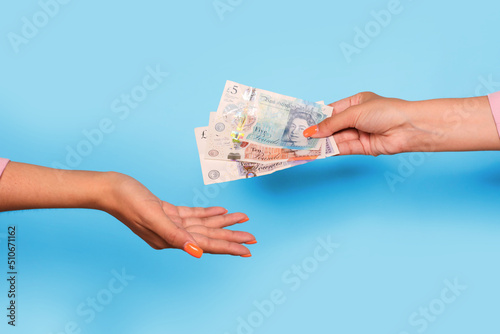 Hand giving united kingdom pounds and hand take, over blue background. Giving money to help