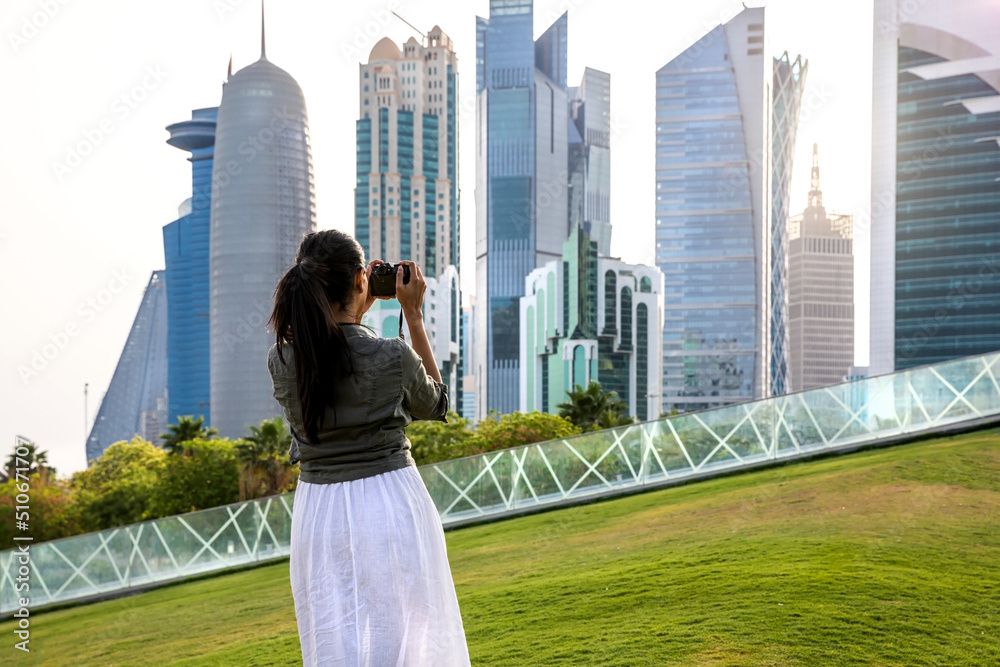 Fototapeta premium Female tourist making photos of the skyline of Doha, Qatar, during sunset time in the park