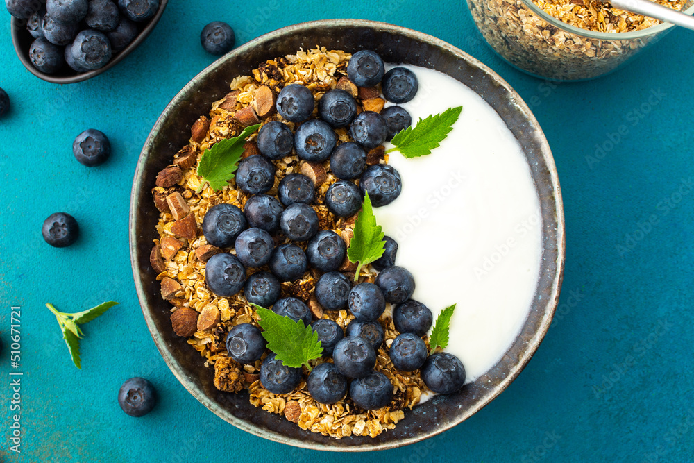 Homemade granola with yogurt, blueberries and mint leaves in a bowl on a turquoise background, delicious healthy breakfast Homemade granola with yogurt, blueberries and mint leaves in a bowl on a turquoise background, delicious healthy breakfast