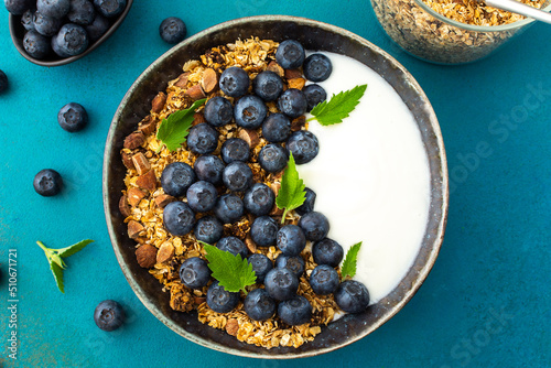 Homemade granola with yogurt, blueberries and mint leaves in a bowl on a turquoise background, delicious healthy breakfast