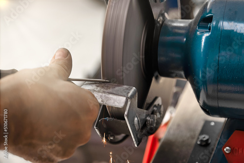 Professional sharpening of tools in a carpentry workshop on a lathe using an abrasive wheel. Sparks from sharpening fly straight down, the master observes safety precautions photo