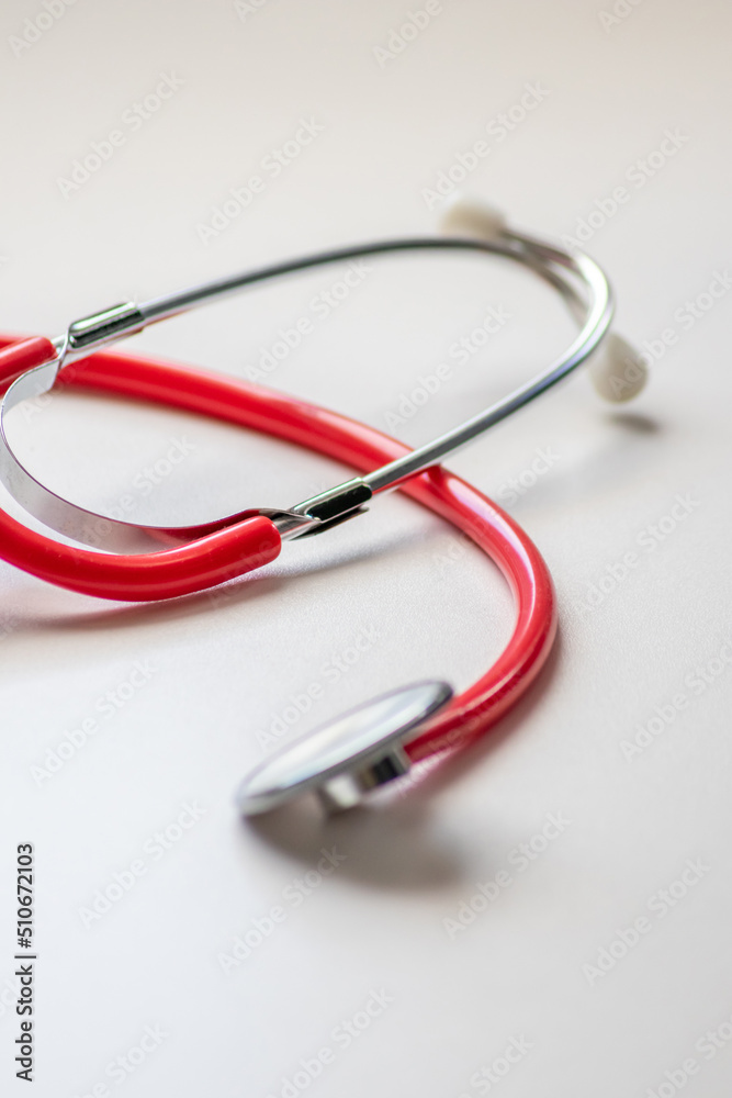 Red stethoscope in doctors office for professional cardio checkup and healthy heartbeat pulse check by cardiologist in clinical treatment room on white desk as medical equipment to measure body params Red stethoscope in doctors office for professional cardio checkup and healthy heartbeat pulse check by cardiologist in clinical treatment room on white desk as medical equipment to measure body params