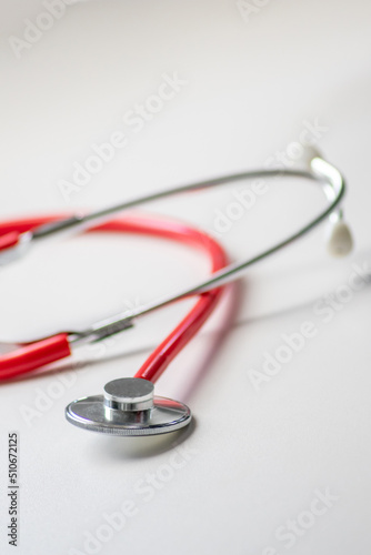 Red stethoscope in doctors office for professional cardio checkup and healthy heartbeat pulse check by cardiologist in clinical treatment room on white desk as medical equipment to measure body params