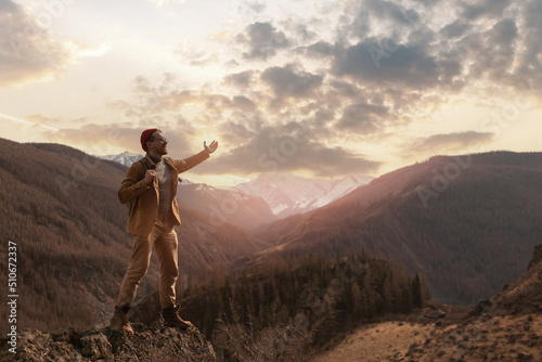 Adventure concept, young happy man with red hat standing on top of cliff mountains background sunset © Parilov