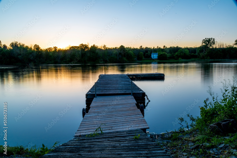 An empty dock sits in the still water of the Trent River during a late evening sunset in Campbellford, Ontario.