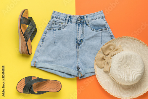 Women's shorts, hat and summer sandals on a yellow and orange background. The minimum concept of summer holidays.