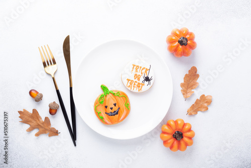 Halloween table setting with gingerbread cookies on white plate and cuterly on white background. Bright homemade cookies for Halloween party photo