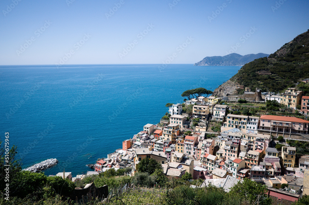 Panoramic view of Riomaggiore town in Cinque Terre National Park, Liguria, Italy. View from above of small touristic village on rocky coastline with typical Italian buildings on Mediterranean coast 