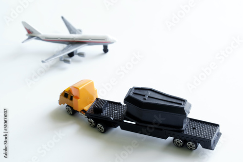 Fototapeta Naklejka Na Ścianę i Meble -  Toy truck with a trailer, an airplane and a coffin on a white background. The concept of transporting the dead and transporting corpses. Toy world. Selective focus.