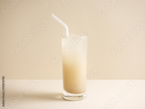 A glass of barley water with straw isolated on grey background side view