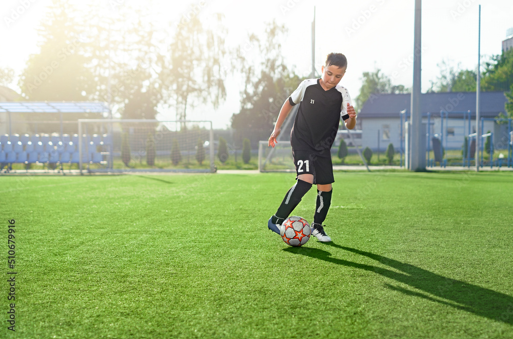 A young man in a black uniform with the number 21 is playing football on the soccer field of the stadium alone. Youth soccer schools. Training and practice in the game A young man in a black uniform with the number 21 is playing football on the soccer field of the stadium alone. Youth soccer schools. Training and practice in the game