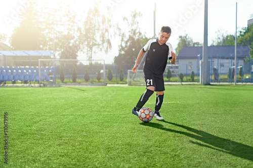 A young man in a black uniform with the number 21 is playing football on the soccer field of the stadium alone. Youth soccer schools. Training and practice in the game