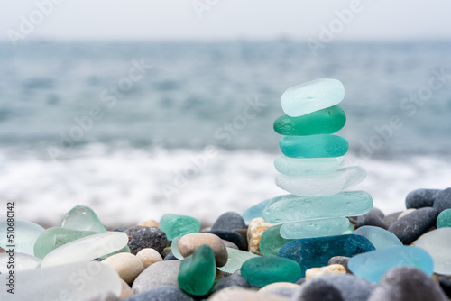 Fototapeta Naklejka Na Ścianę i Meble -  Natural polish textured sea glass and stones on the seashore. Azure clear sea water with waves. Green, blue shiny glass with multi-colored sea pebbles close-up. Beach summer background