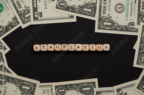 the word stagflation laid with wooden cubes on black background with dollar banknotes and means recession-inflation photo