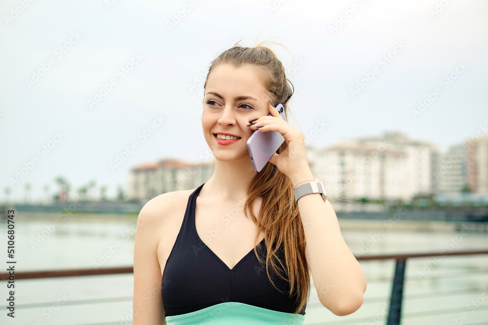 Happy brunette woman wearing black sports bra standing on city park, outdoors talking on mobile phone with friends or boyfriend with smiles. Happy brunette woman wearing black sports bra standing on city park, outdoors talking on mobile phone with friends or boyfriend with smiles.