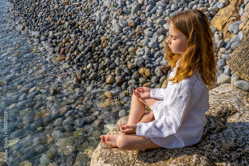 Beautiful little girl sitting on a rock by the sea and meditate