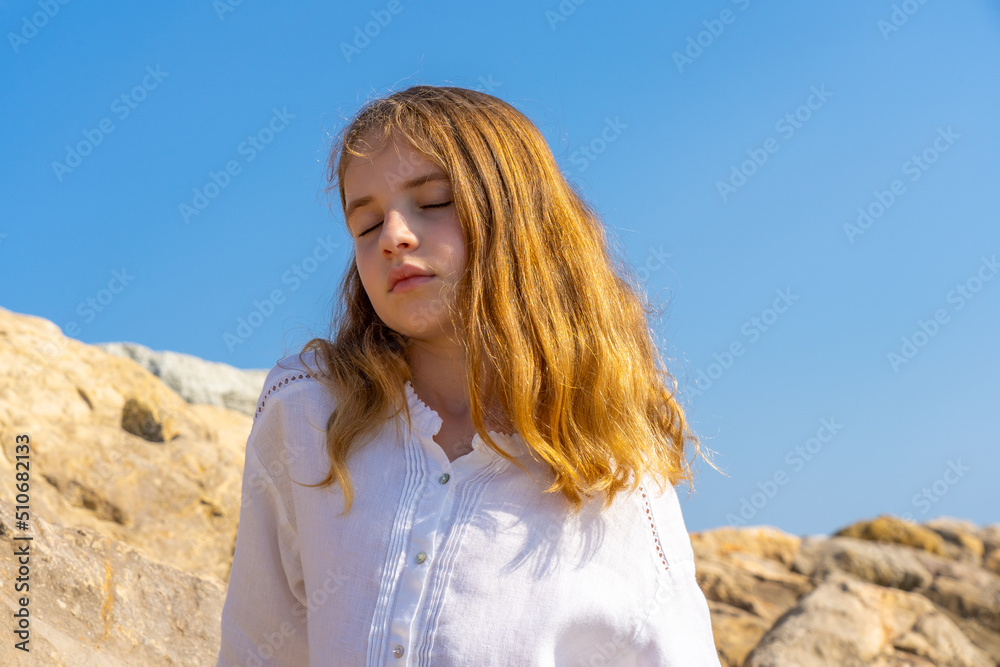 Beautiful little girl standing on a rock by the sea with closed eyes and dreaming Beautiful little girl standing on a rock by the sea with closed eyes and dreaming