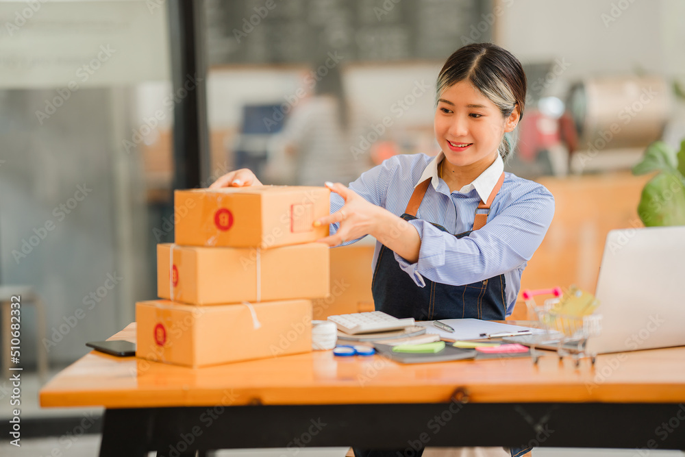 Asian women SME small business entrepreneurs online selling ideas Happy Young Asian business owner working on computers and boxes at home. Deliver SME parcel boxes to customers horizontally Asian women SME small business entrepreneurs online selling ideas Happy Young Asian business owner working on computers and boxes at home. Deliver SME parcel boxes to customers horizontally