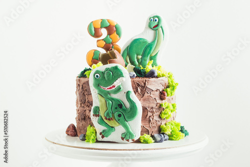 Birthday cake for a little fan of dinosaurs on the white background. Cake with brown rustic cream cheese frosting and gingerbread cookies