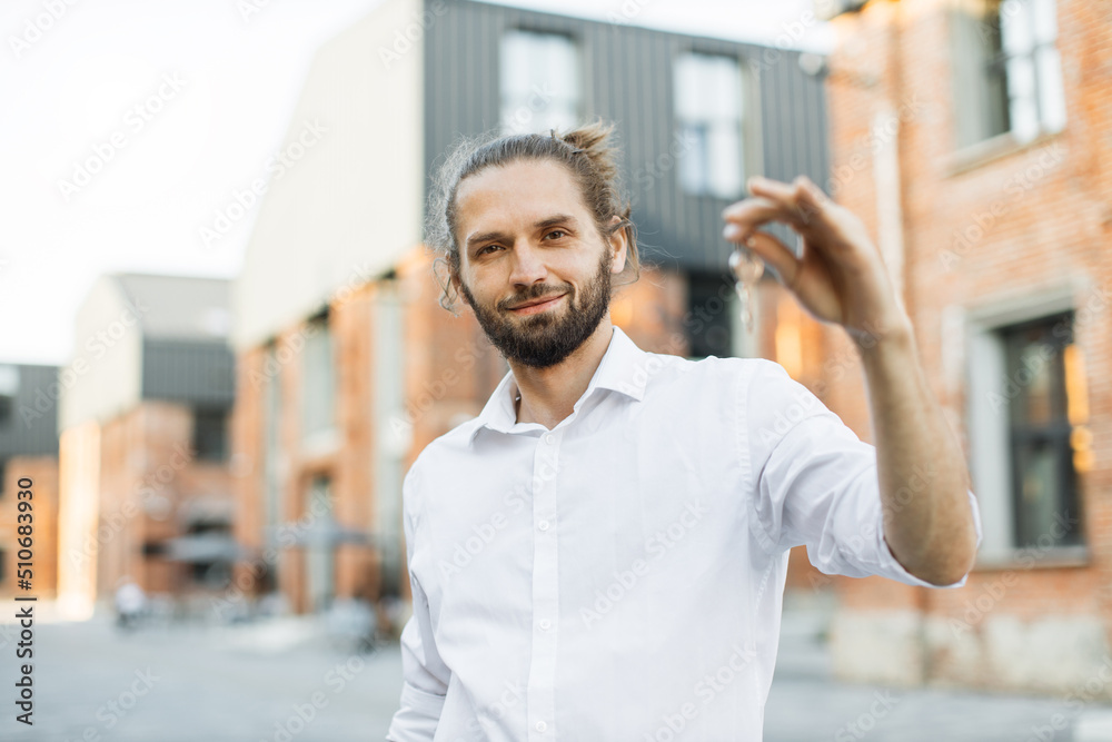 Real estate attractive agent beautiful man with house keys in front of sold apartment, in city street. Young caucasian guy in white shirt with keys just bought new apartment. Real estate attractive agent beautiful man with house keys in front of sold apartment, in city street. Young caucasian guy in white shirt with keys just bought new apartment.