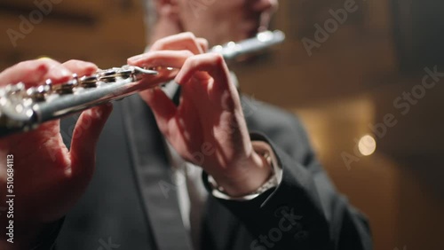 professional flutist is playing flute in philharmonic hall, rehearsal or concert of symphonic orchestra, closeup photo