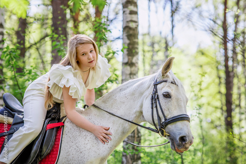 Teenage girl with her favorite white horse for a walk in the spring forest. Communication with animals in nature. Horizontal photographs of animals.