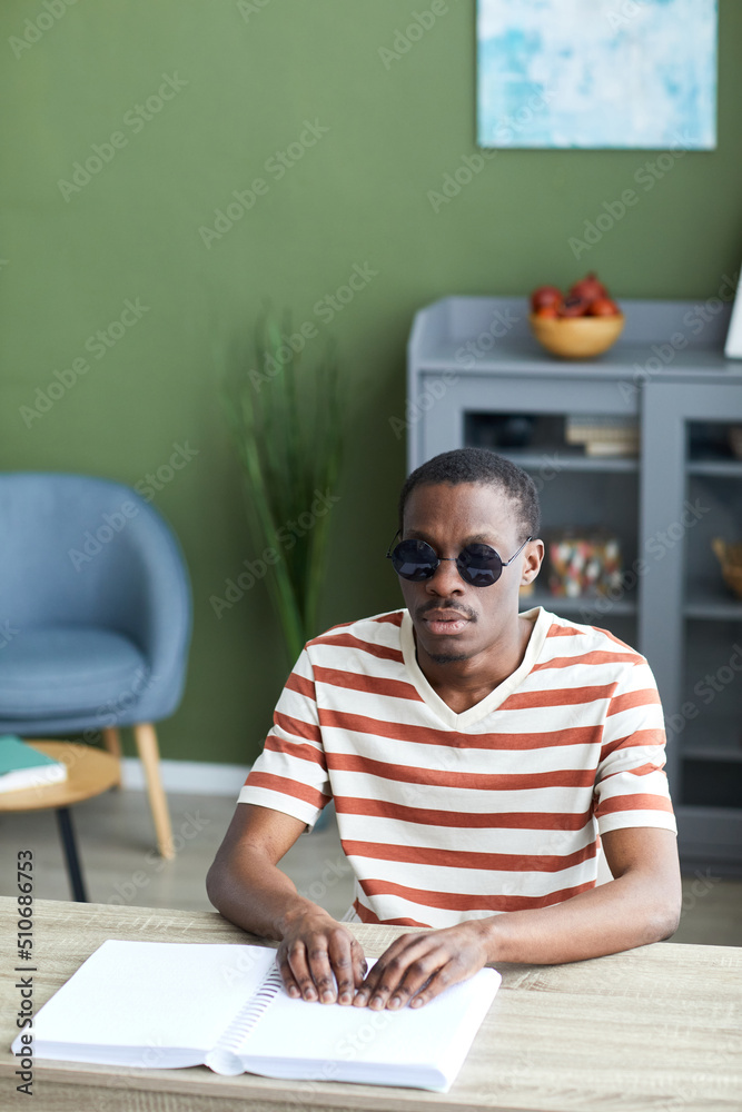 Vertical portrait of adult black man reading tactile book in braille and wearing dark sunglasses, accessible information concept Vertical portrait of adult black man reading tactile book in braille and wearing dark sunglasses, accessible information concept