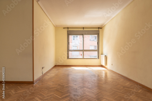 Empty living room with oak parquet flooring, aluminum radiator in one corner and brown aluminum window