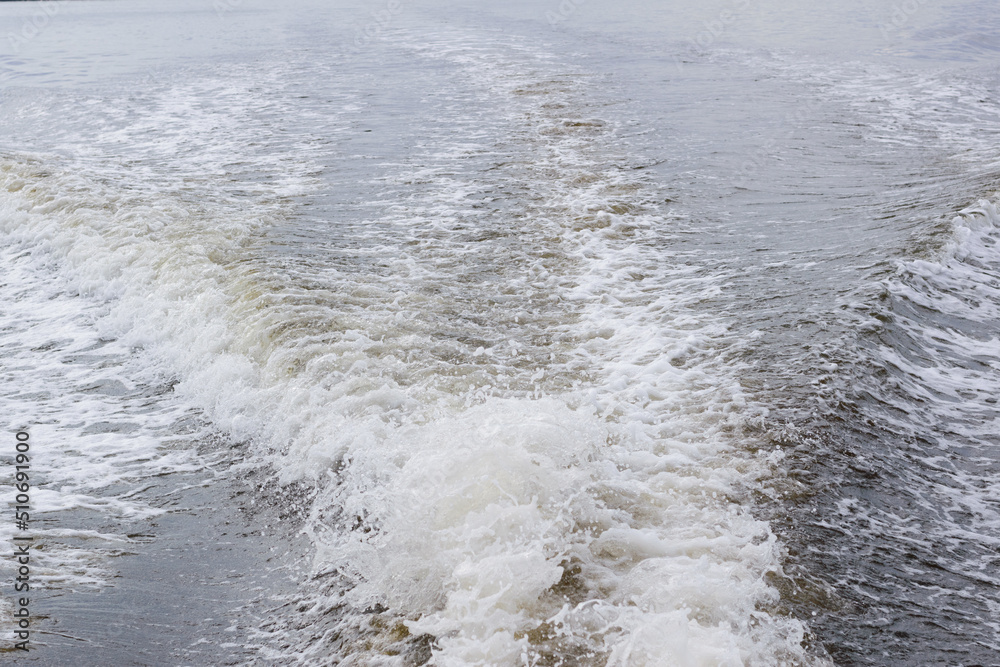 Back of speedboat with a view of wake trailing behind the motor with white foam on the edge of the wave