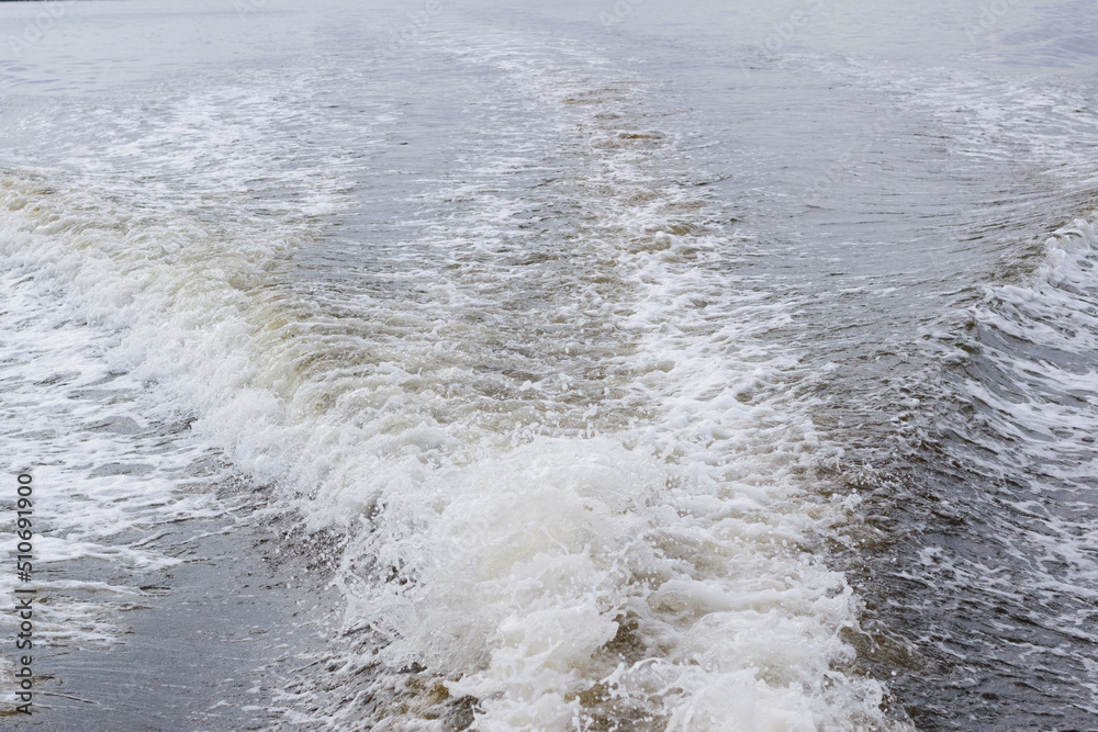 Back of speedboat with a view of wake trailing behind the motor with white foam on the edge of the wave Back of speedboat with a view of wake trailing behind the motor with white foam on the edge of the wave