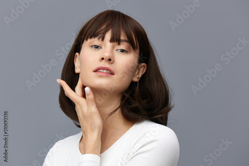 a beautiful woman stands full-face on a dark background in a white tight T-shirt, put her hand on her face, looking gently forward