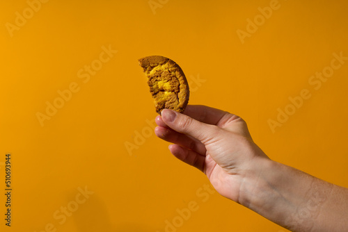 half a cookie in a human hand close-up on a yellow background