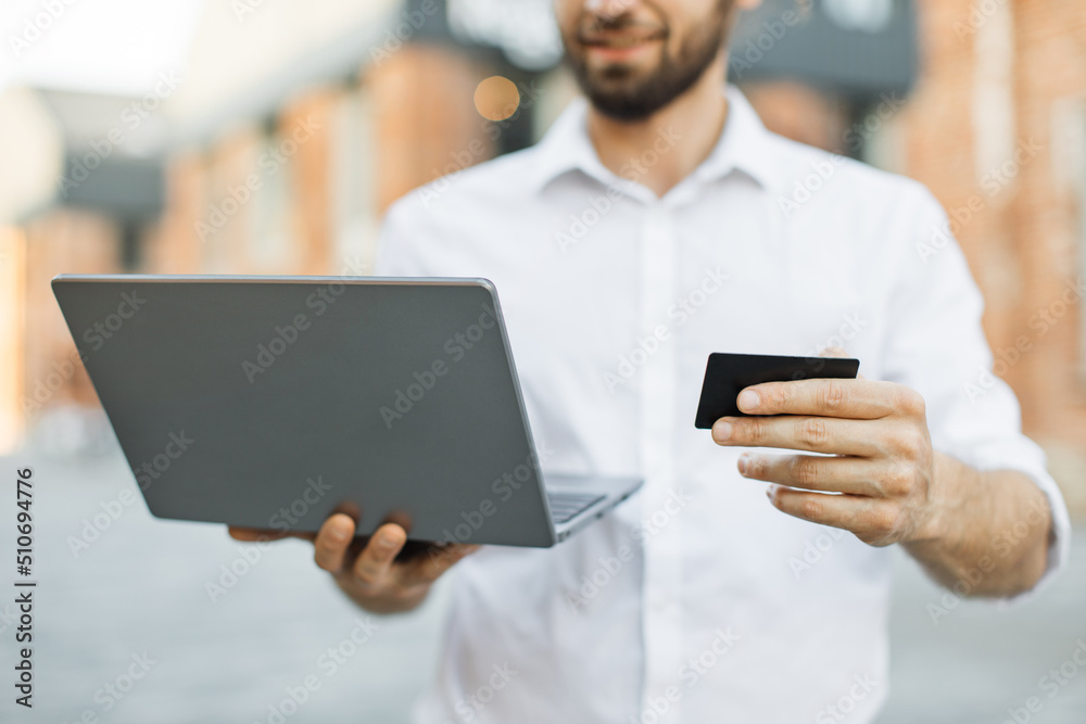 Focus on laptop and bank card. Business trip concept. Handsome young man, using notebook and holding credit card for shopping online. Male freelancer receive payment online.