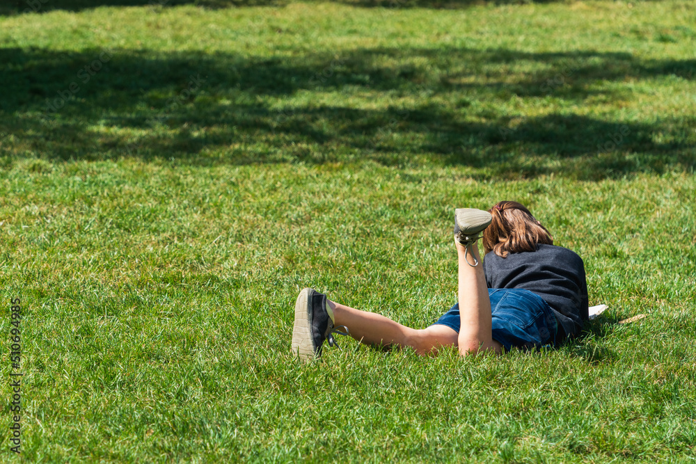 A school-age girl reads a book while lying on the grass in a city park on a sunny Sunday afternoon. Children's self-education in their free time, the importance of reading A school-age girl reads a book while lying on the grass in a city park on a sunny Sunday afternoon. Children's self-education in their free time, the importance of reading