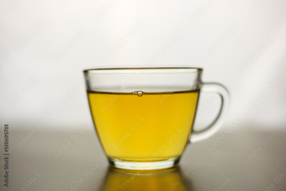 Brewed herbal green tea in a transparent cup on a dark table with a bright white light on the background Brewed herbal green tea in a transparent cup on a dark table with a bright white light on the background