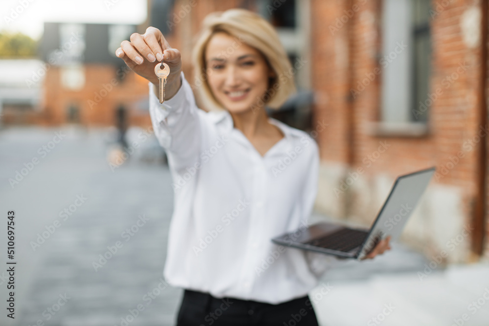 Focuse on woman hand with keys. Real estate attractive agent beautiful woman with house keys and laptop in front of sold apartment, in city street. Focuse on woman hand with keys. Real estate attractive agent beautiful woman with house keys and laptop in front of sold apartment, in city street.