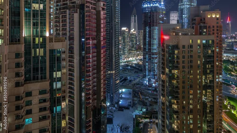 Aerial cityscape night timelapse with illuminated architecture of Dubai downtown. Many tall skyscrapers and towers with glowing windows. New construction site.